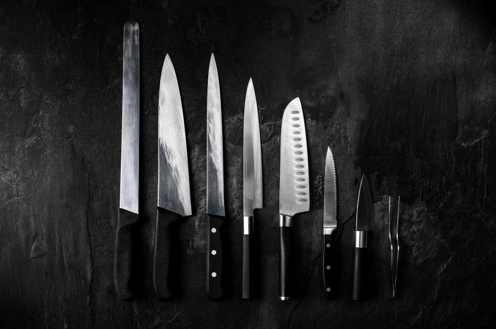 Set of professional kitchen knives and tweezers on dark stone background. Creative layout. Chef, restaurant or kitchen concept. 