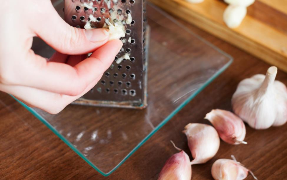 grating garlic on top of a glass cutting board
