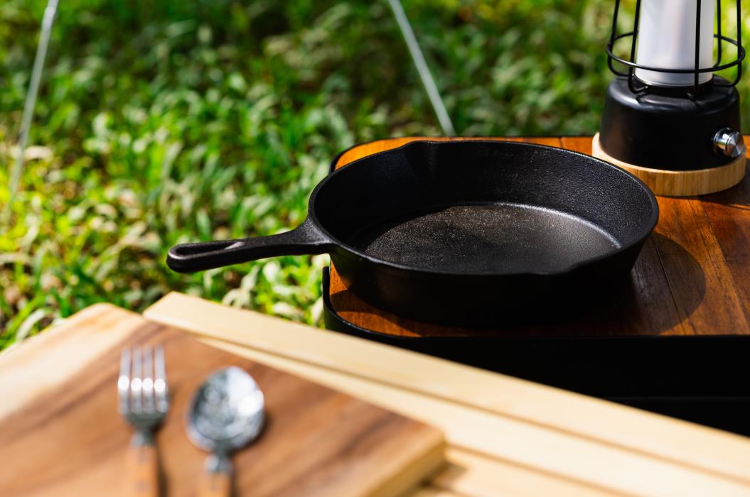 Iron pan and camping accessory on wood table. Equipment for camping in forest. In summer with sunlight.