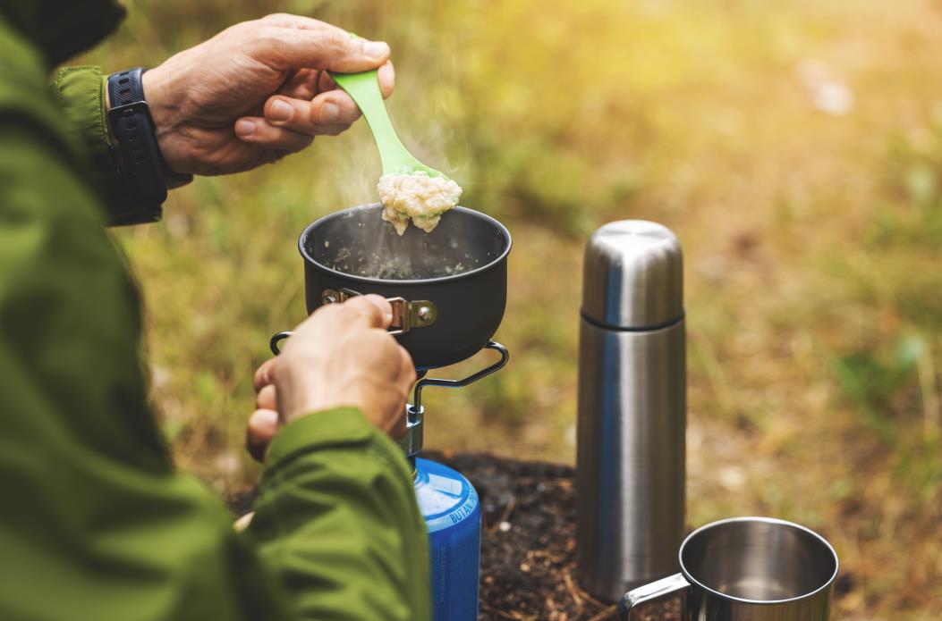 preparing oatmeal porridge outdoors on gas burner. camping cooking equipment